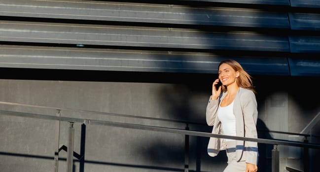 Young business woman strolls through a contemporary outdoor space, exuding confidence while dressed in sleek attire. The warm light accentuates her stylish presence