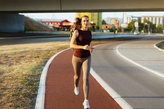 An energetic woman jogs gracefully on a winding trail, illuminated by the warm hues of sunset, surrounded by an urban landscape and modern architecture