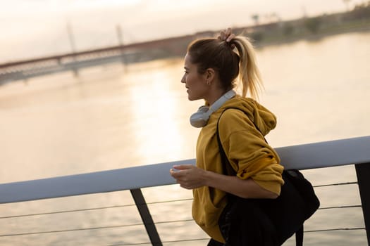 A carefree woman walks along a contemporary riverside path, her cheerful demeanor captured as she enjoys the picturesque sunset and fresh air.