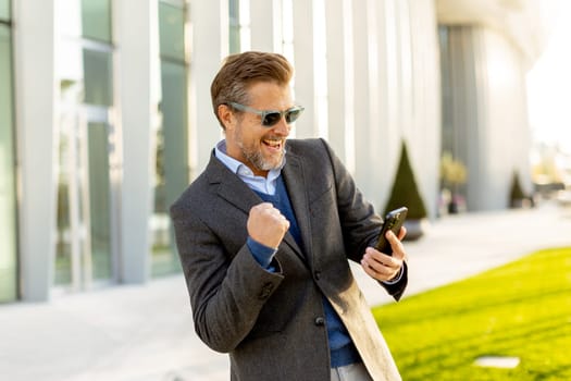 A cheerful man in a fashionable suit and sunglasses laughs heartily, gesturing with excitement while enjoying a lively moment outside in an urban landscape.