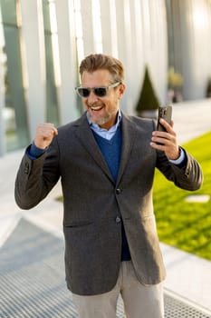A cheerful man in a fashionable suit and sunglasses laughs heartily, gesturing with excitement while enjoying a lively moment outside in an urban landscape.