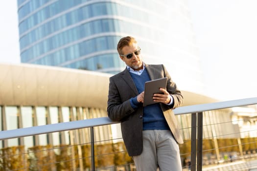 An elegant individual in a blazer stands on a balcony at sunset, holding a tablet and gazing over a vibrant metropolis, embodying professionalism and relaxation.