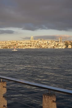 Calm waters reflect the skyline of a city at sunset while boats pass by.