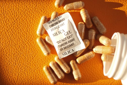 Silica gel capsules and a warning packet rest on an orange background.
