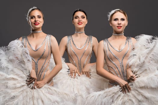 Three dancers in glamorous outfits display their beauty and skill while posing together, highlighting intricate designs and dynamic expressions.