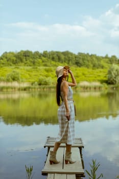 Young woman standing on the wooden pier at the calm lake on a hot summer day
