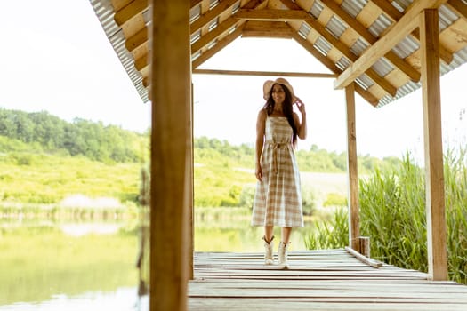 Young woman walking on the wooden pier at the calm lake on a hot summer day