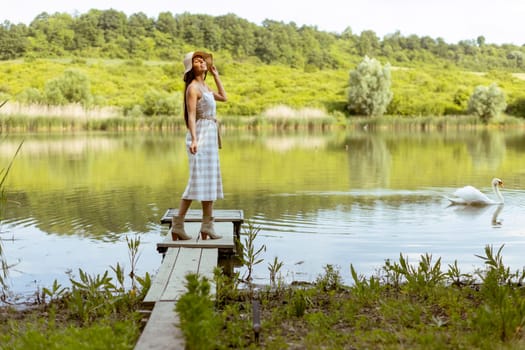 Young woman standing on the wooden pier at the calm lake on a hot summer day