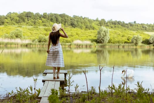 Young woman standing on the wooden pier at the calm lake on a hot summer day