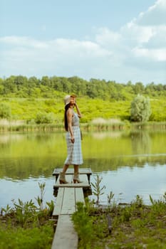 Young woman standing on the wooden pier at the calm lake on a hot summer day