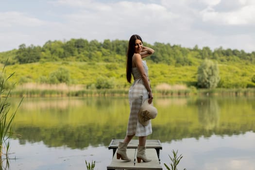 Young woman standing on the wooden pier at the calm lake on a hot summer day