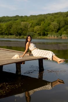 Young woman relaxing on the wooden pier at the calm lake on a hot summer day