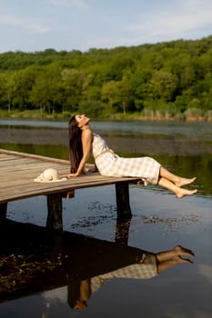 Young woman relaxing on the wooden pier at the calm lake on a hot summer day