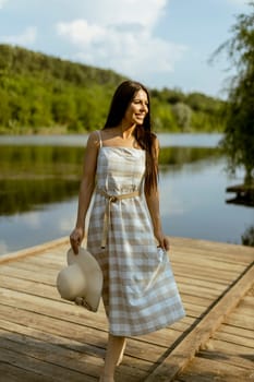 Young woman walking on the wooden pier at the calm lake on a hot summer day
