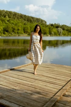 Young woman walking on the wooden pier at the calm lake on a hot summer day