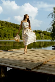Young woman walking on the wooden pier at the calm lake on a hot summer day