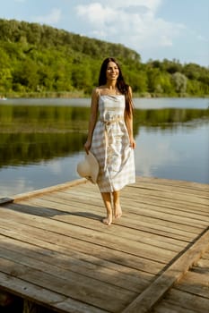 Young woman walking on the wooden pier at the calm lake on a hot summer day