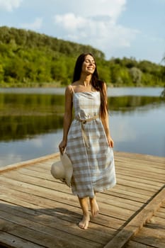 Young woman walking on the wooden pier at the calm lake on a hot summer day
