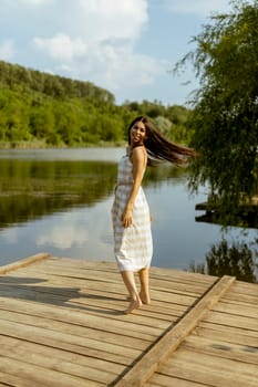 Young woman walking on the wooden pier at the calm lake on a hot summer day