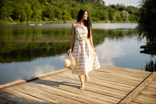 Relaxing young woman standing on wooden pier at the calm lake