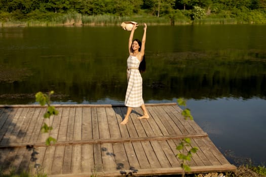Happy young woman standing on the wooden pier at the calm lake on a hot summer day