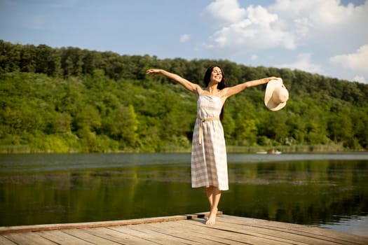 Relaxing young woman standing on wooden pier at the calm lake