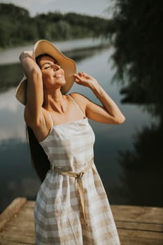 Relaxing young woman standing on wooden pier at the calm lake