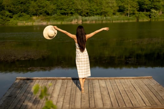 Happy young woman standing on the wooden pier at the calm lake on a hot summer day