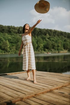 Happy young woman standing on wooden pier at the calm lake