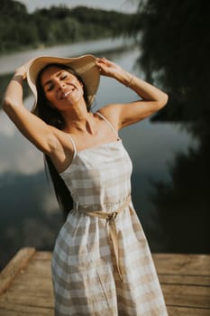 Relaxing young woman standing on wooden pier at the calm lake