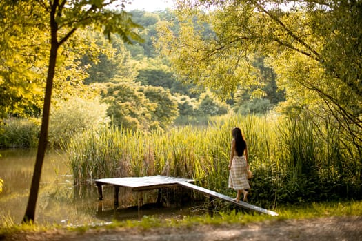 Young woman walking on the wooden pier at the calm lake on a hot summer day