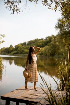 Young woman standing on the wooden pier at the calm lake on a hot summer day