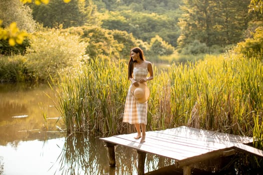 Young woman standing on the wooden pier at the calm lake on a hot summer day