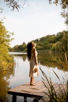 Young woman standing on the wooden pier at the calm lake on a hot summer day