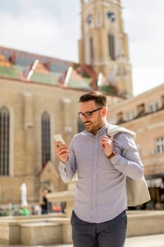 Cheerful young man uses mobile phone in urban enviroment at sunny day