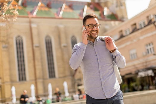 Cheerful young man uses mobile phone in urban enviroment at sunny day