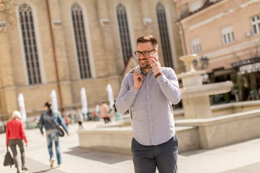 Cheerful young man uses mobile phone in urban enviroment at sunny day