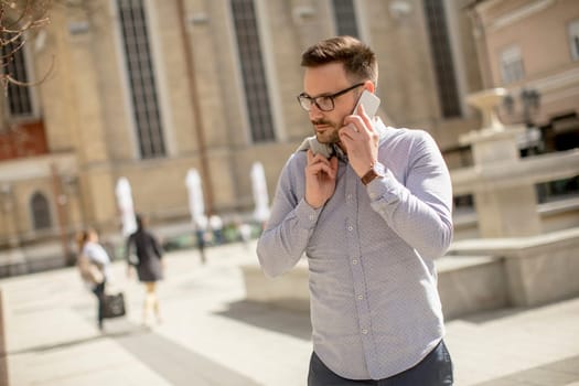 Cheerful young man uses mobile phone in urban enviroment at sunny day