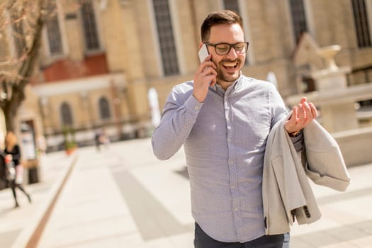 Cheerful young man uses mobile phone in urban enviroment at sunny day