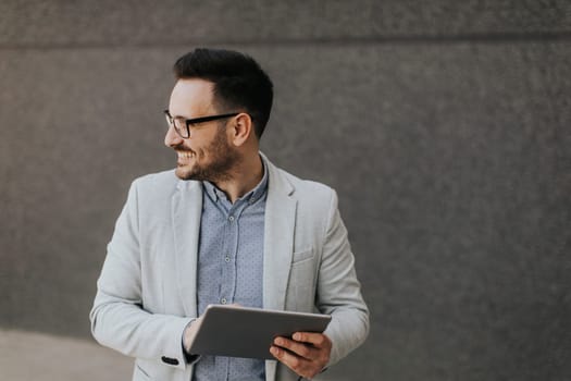 Handsome young businessman with digital tablet by the grey wall