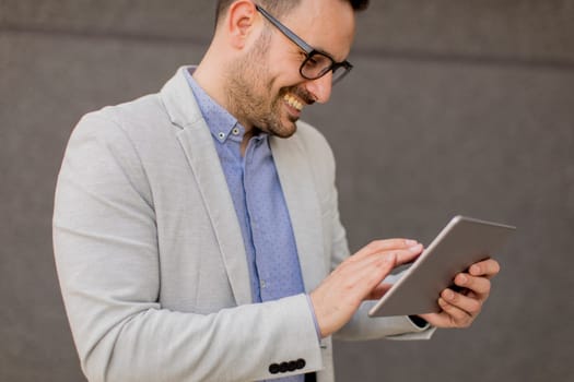 Handsome young businessman with digital tablet by the grey wall