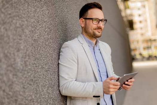 Handsome young businessman with digital tablet by the grey wall