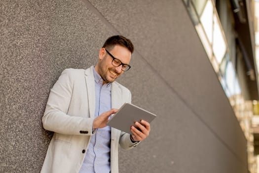 Handsome young businessman with digital tablet by the grey wall