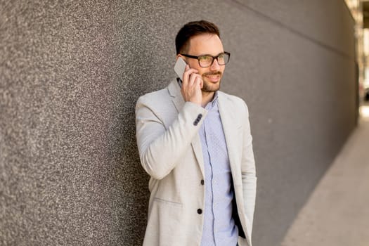 Handsome young businessman with mobile phone by the grey wall