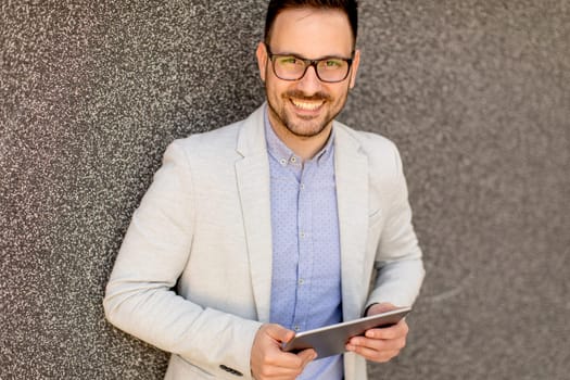 Handsome young businessman with digital tablet by the grey wall