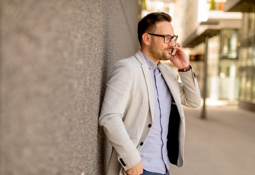 Handsome young businessman with mobile phone by the grey wall