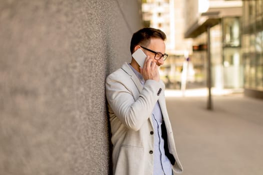 Handsome young businessman with mobile phone by the grey wall