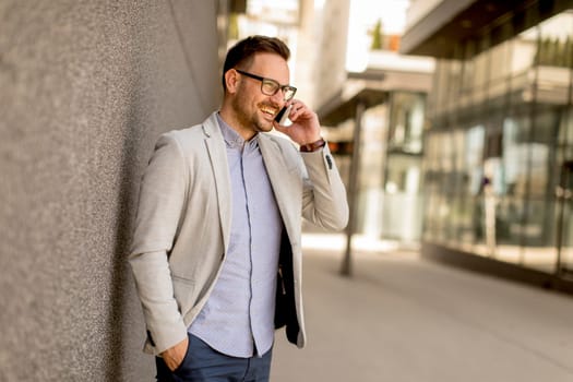Handsome young businessman with mobile phone by the grey wall