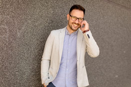 Handsome young businessman with mobile phone by the grey wall