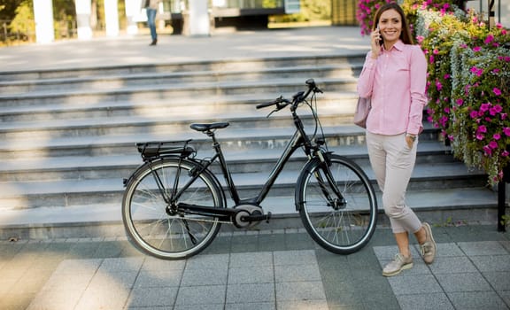 Young woman standing near ebike and uses smartphone outdoor